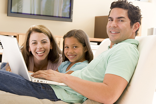Families In Living Room With Laptop Smiling